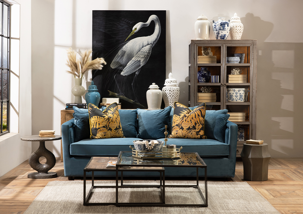 Blue velvet sofa styled with asian-inspired display cabinet, industrial-style coffee table and ginger jars