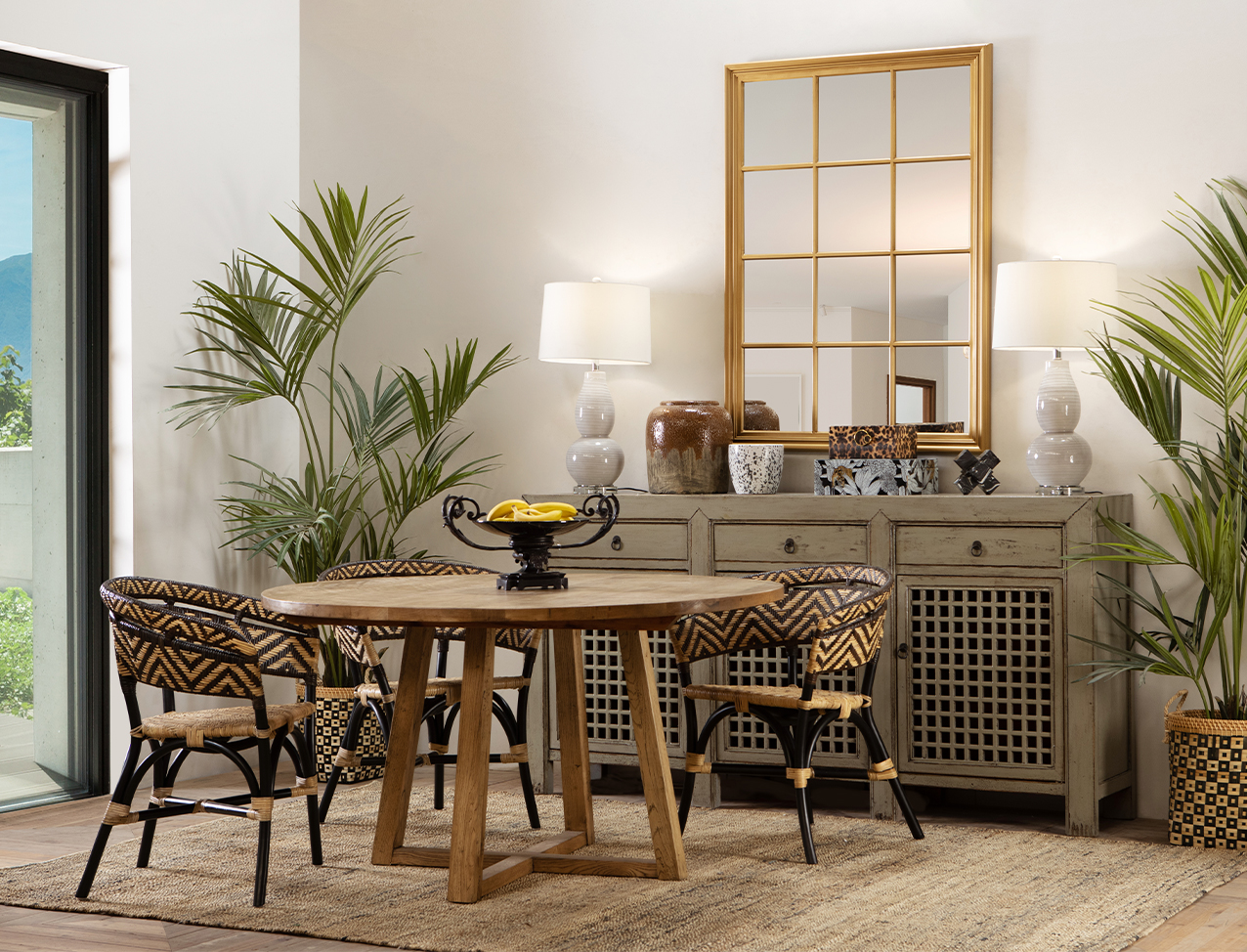 Round wooden dining table in eclectic decor scene with Asian-inspired sideboard and African-inspired pattern rattan dining chairs